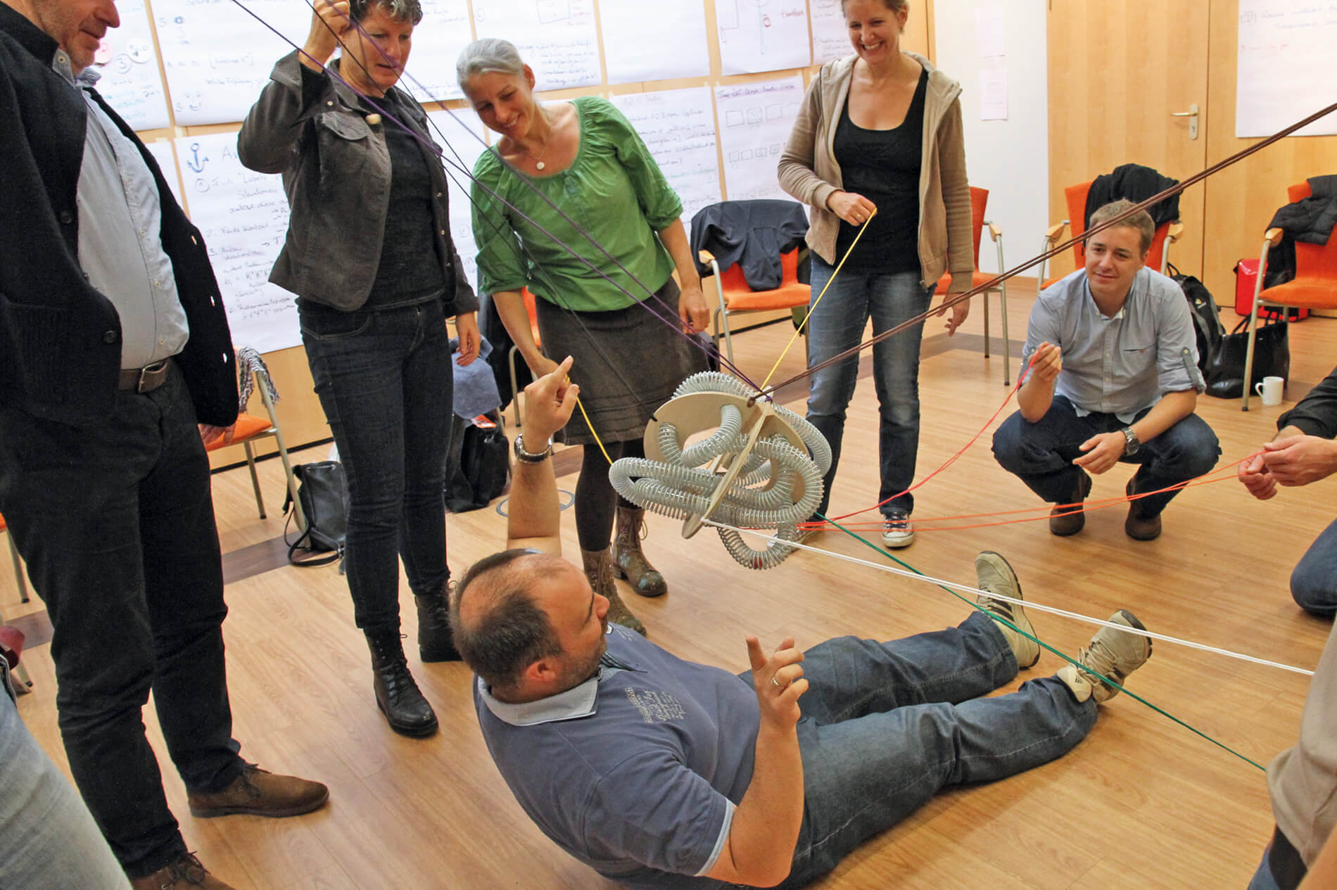 A trainer crouches beneath PerspActive coaching six adults in a fun team building activity