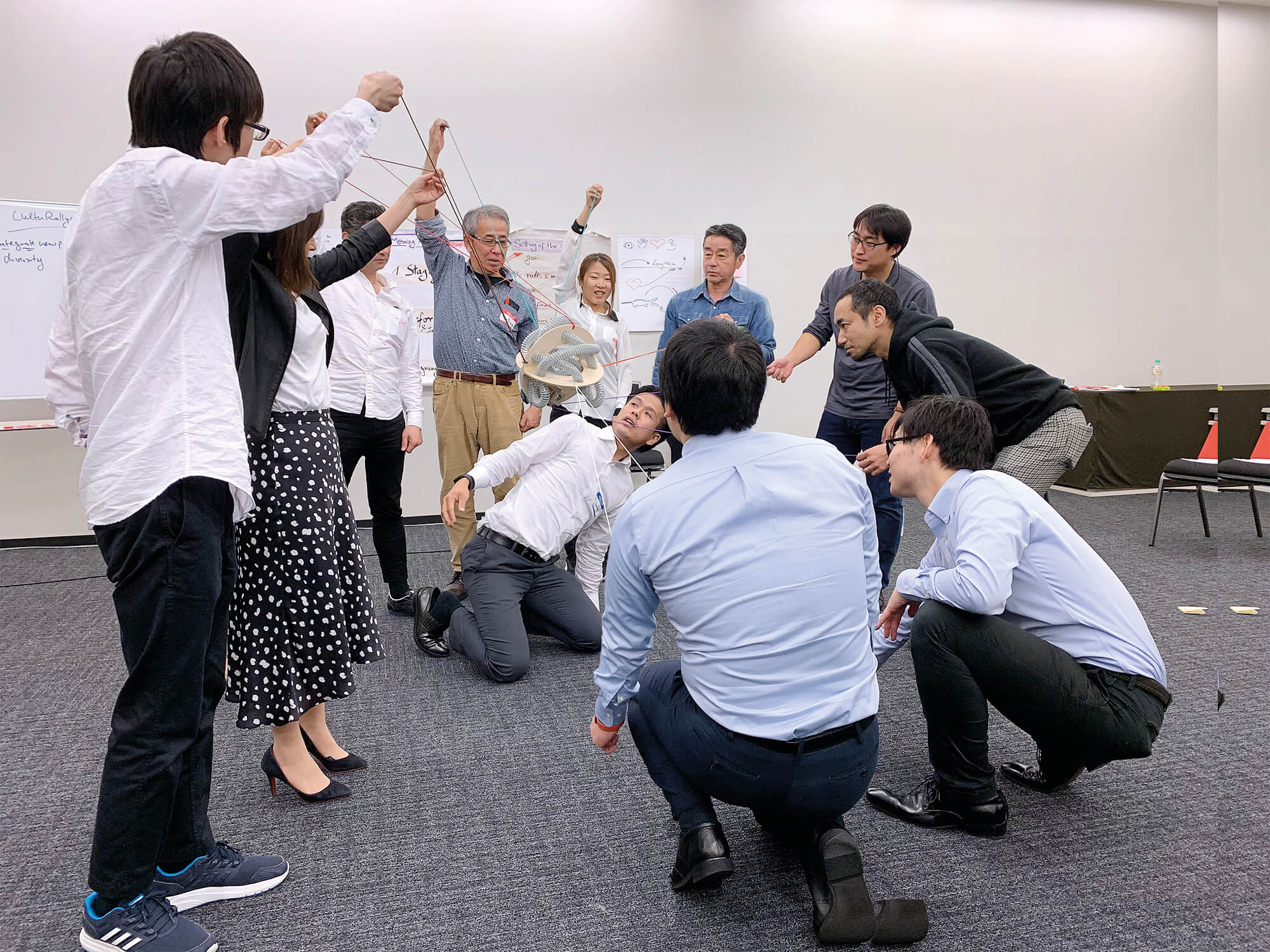 Ten adults in office attire use PerspActive, a team activity made of a 15-inch sphere and 12 strings