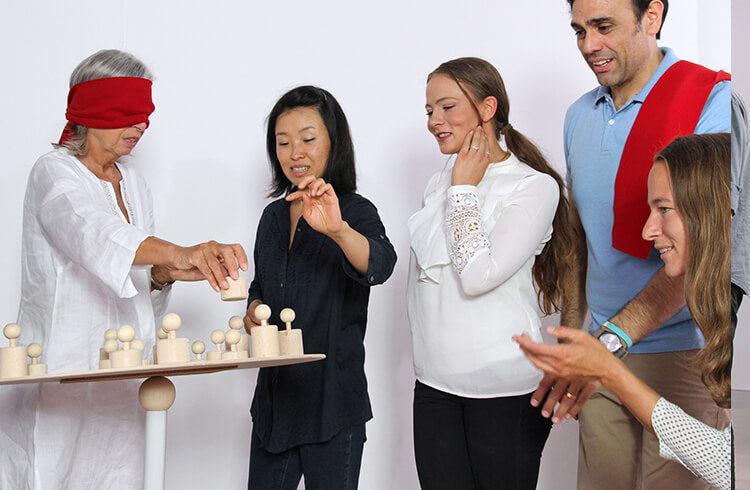 A trainer instructs a blindfolded learner where to place a figurine in Metalog SysTeam activity