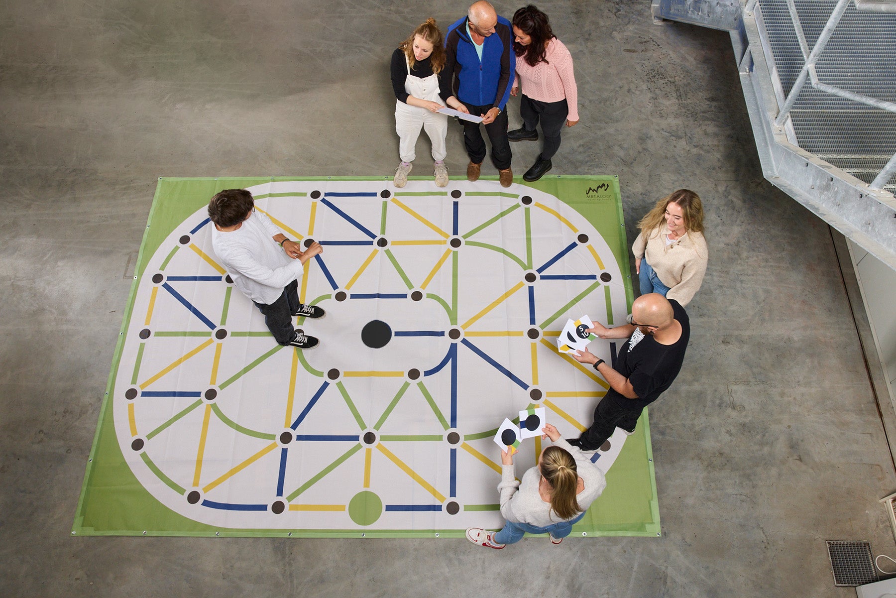 Seven adults stand on or near a color maze set on a concrete floor