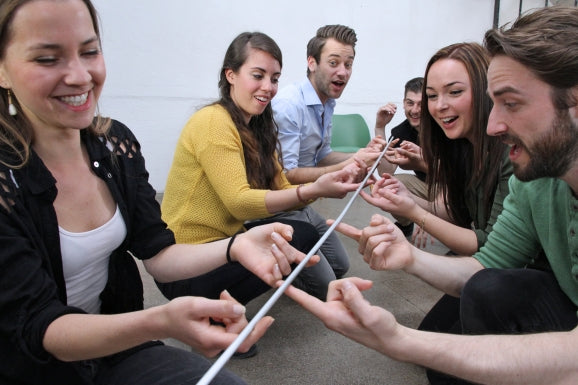 A small team of workplace colleagues uses FloatingStick to practice team interdependence.