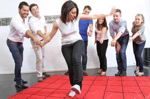 A worker is directed by her coworkers how to walk across a red floor mat called The Maze.