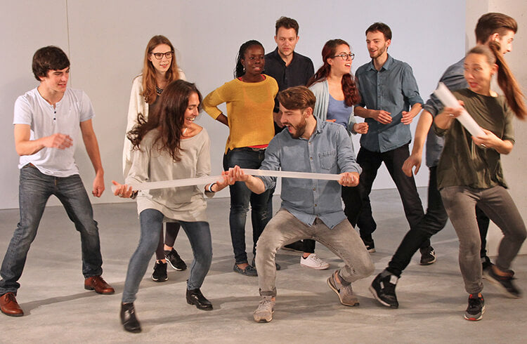 Ten young adults smile and have fun keeping a ball rolling through half pipes with Metalog Pipeline