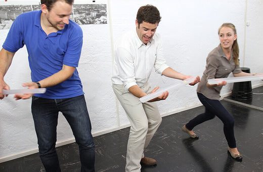 Three young adults work quickly to keep a ball rolling through Pipeline, a team building game